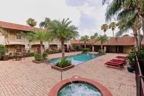 A pool area with a hot tub, lounge chairs, and palm trees.