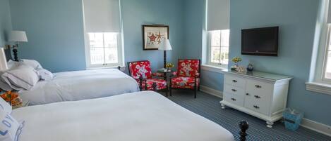 A hotel room with two beds, a red floral armchair, a white dresser, and a television mounted on the wall.
