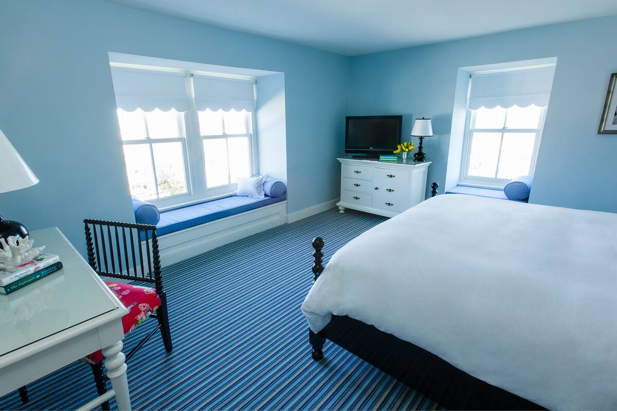 A bedroom with a bed, a desk with a chair, a television, and a window seat.