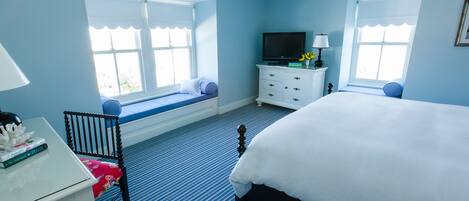 A bedroom with a bed, a desk with a chair, a television, and a window seat.