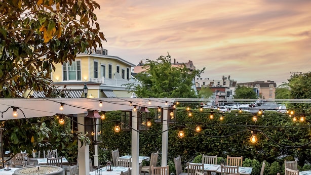 An outdoor dining area with tables and chairs, string lights, and a pergola.