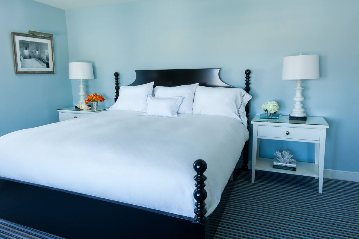 A neatly made bed with white linens, two bedside tables with lamps, and a framed picture on the wall.