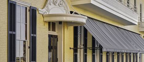 Un edificio amarillo con balcón, mesas al aire libre y un toldo a rayas.