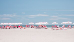 A beach with rows of pink and white beach chairs and umbrellas, and a clear blue sky.