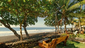A beachside seating area with a stone wall, wooden furniture, and a view of the ocean. - Terraza Del Pacifico Hotel (Jacó)