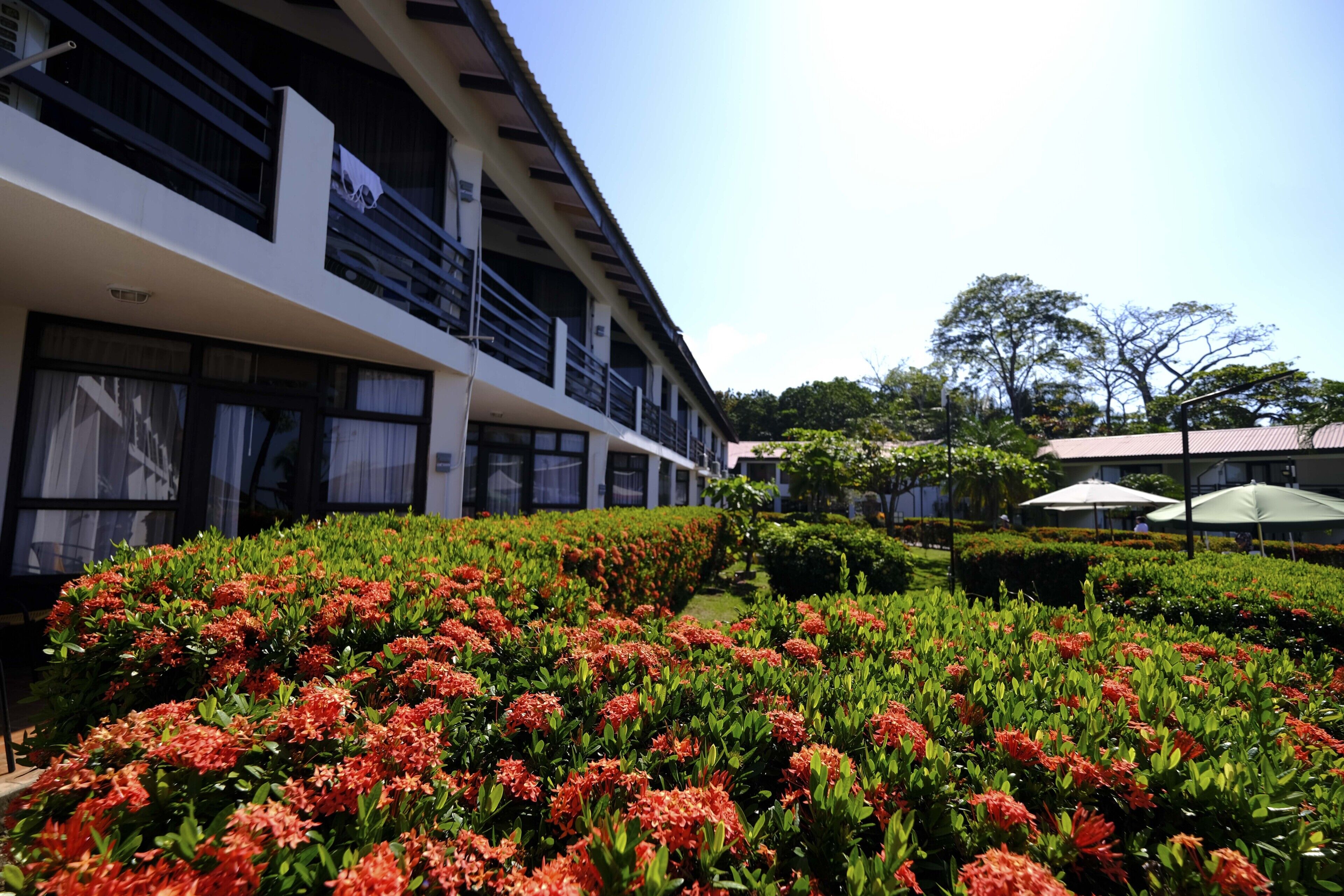 A hotel with a modern design, featuring a large balcony area and a well-maintained garden with vibrant flowers.