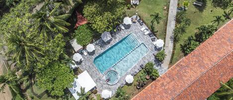 An aerial view of a resort with a swimming pool, lounge area, and tropical landscaping.