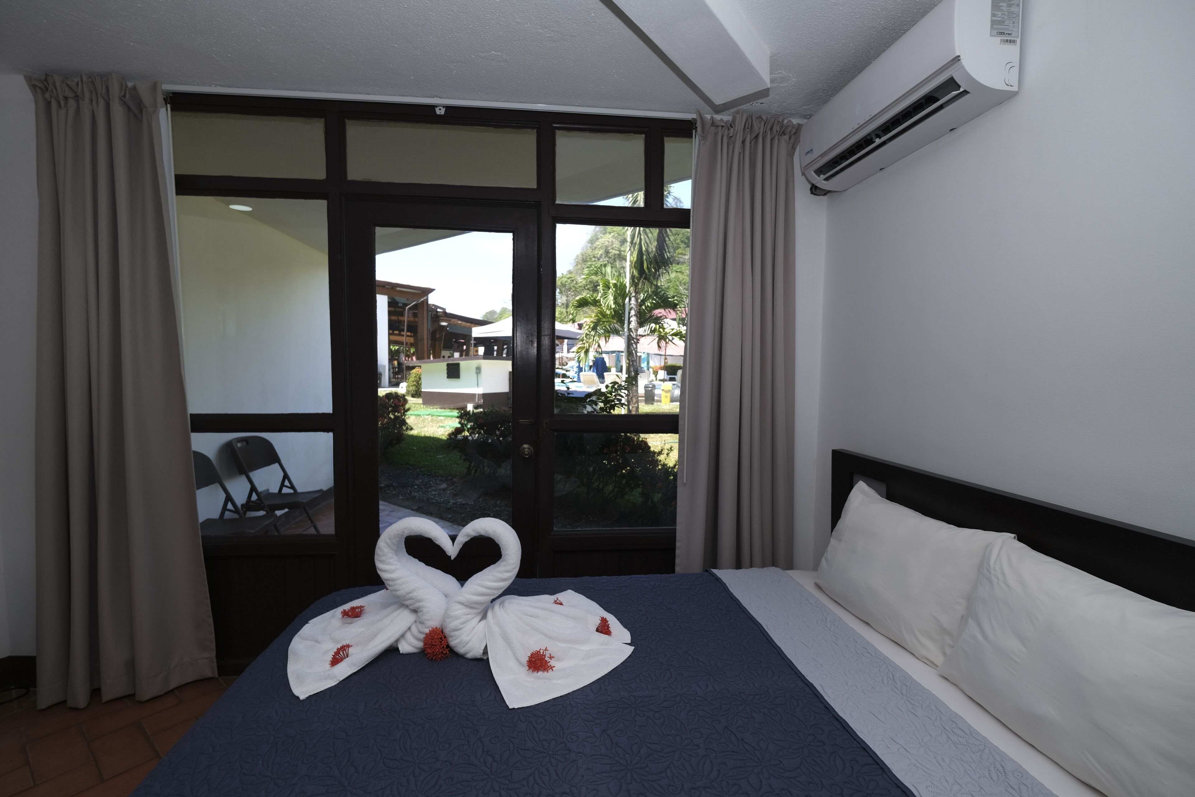 Una habitación de hotel con una cama, un ventanal grande y un equipo de aire acondicionado.