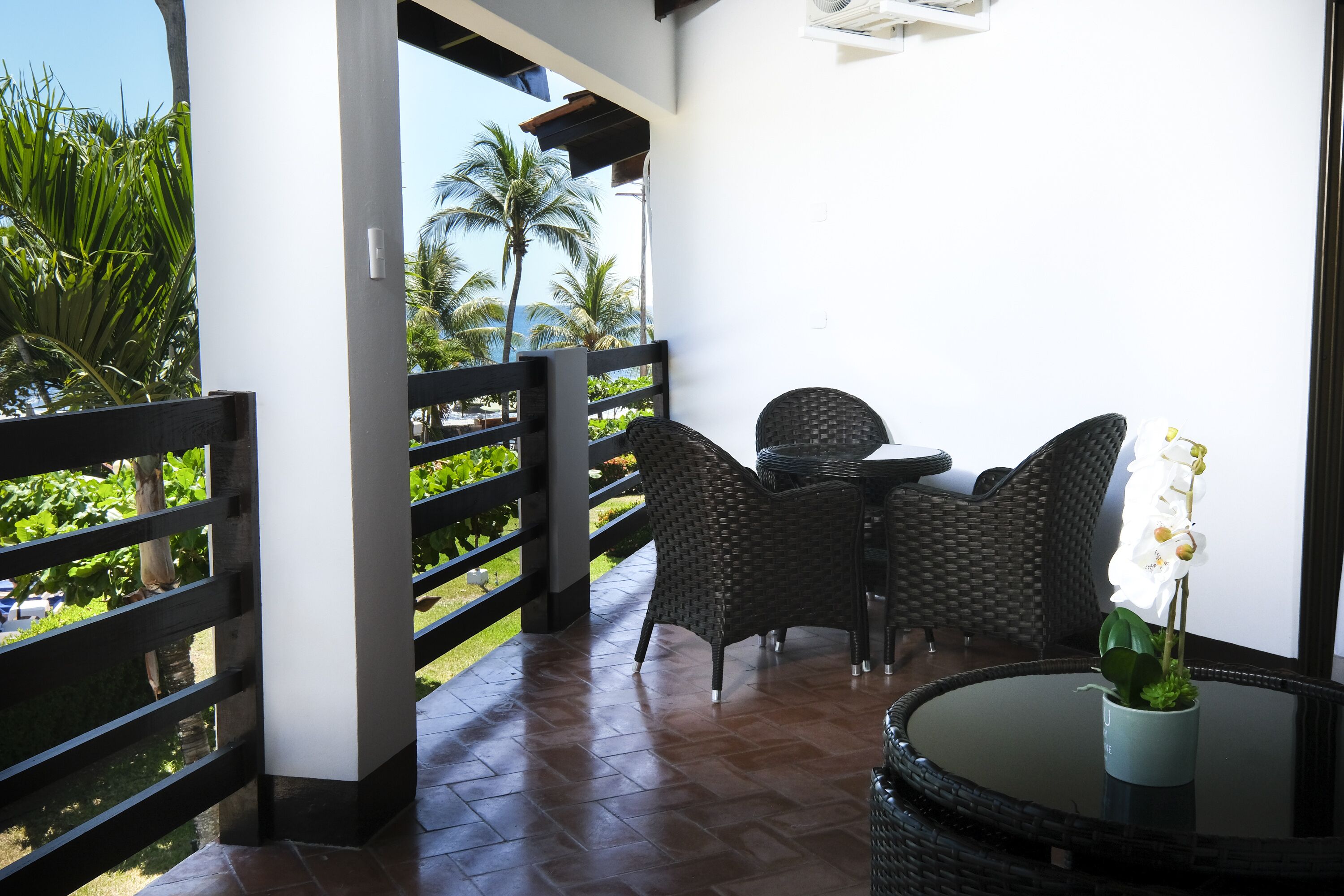 A balcony with wicker furniture, a glass table, and a potted orchid.