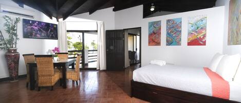 A room with a bed, a dining table with chairs, a TV, and artwork on the walls.