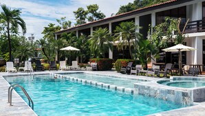 A swimming pool with lounge chairs and umbrellas, surrounded by palm trees and a building with balconies. - Terraza Del Pacifico Hotel (Jacó)