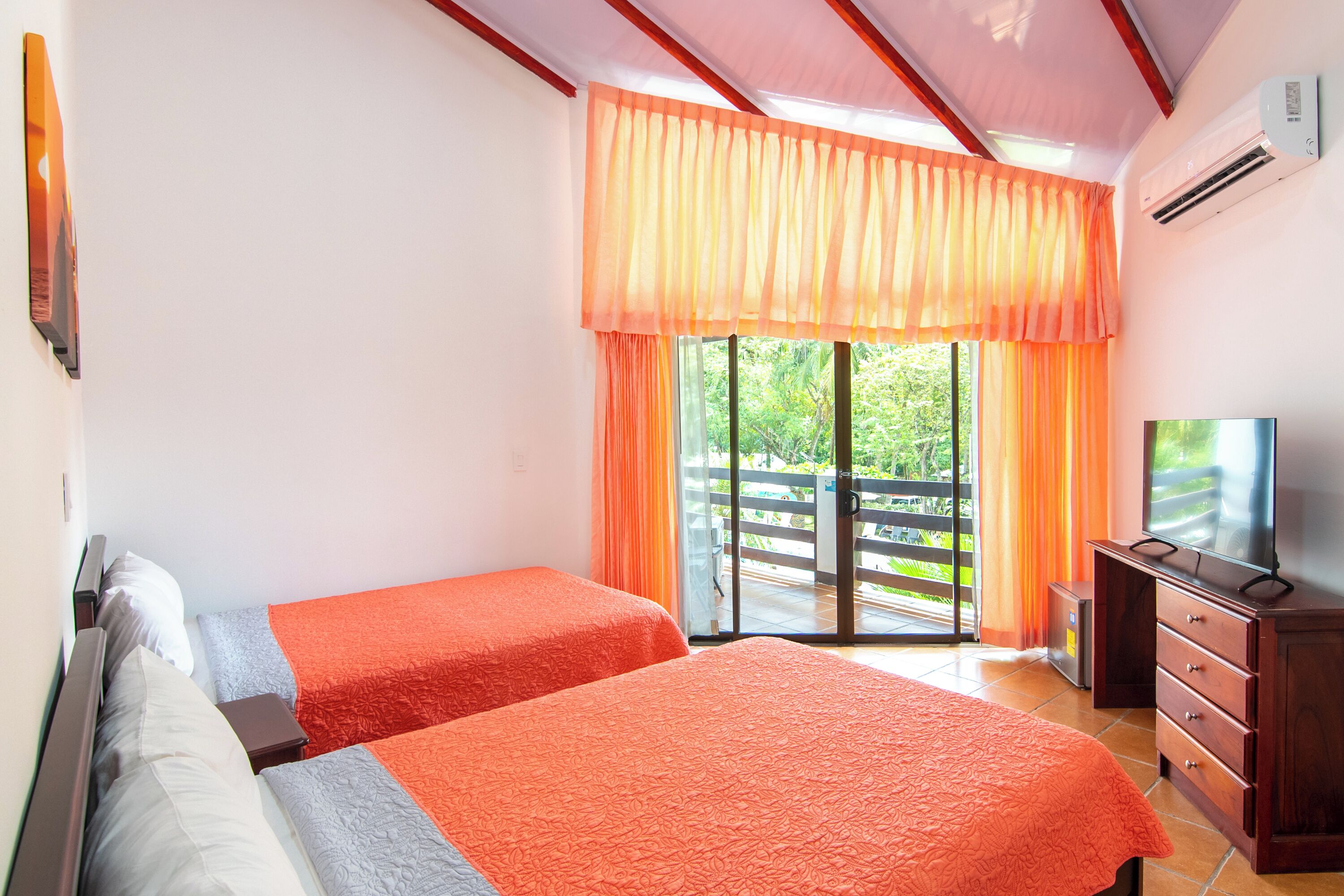 Ein Hotelzimmer mit zwei Betten, einem Fernseher, einem Schminktisch und einer Glastür zum Balkon.