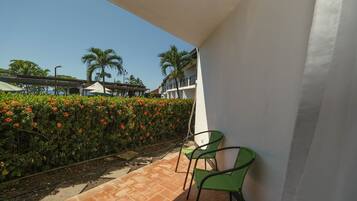 A balcony with two green chairs, a tiled floor, and a hedge with red flowers.