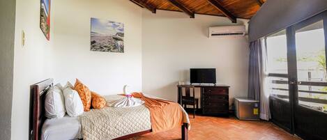A bedroom with a bed, a TV, an air conditioner, and a balcony with a view.