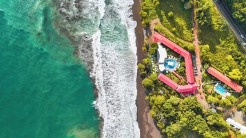 An aerial view of a coastal resort with a swimming pool, beach access, and lush greenery.