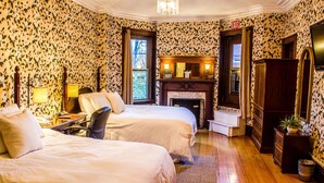 A hotel room with two beds, a fireplace, a mirror, and a wooden floor. - Beacon Inn 1087 (Brookline)