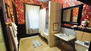 A bathroom with a bathtub, a sink, and a toilet. There is a shower curtain, a towel rack, and a rug on the floor. - Beacon Inn 1087 (Brookline)