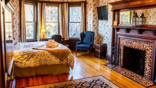 A bedroom with a bed, a chair, a fireplace, and a television. - Beacon Inn 1087 (Brookline)