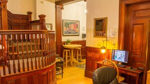 A well-lit room with a wooden staircase, a round table with stools, a computer desk with a chair, and a framed picture on the wall. - Beacon Inn 1087 (Brookline)