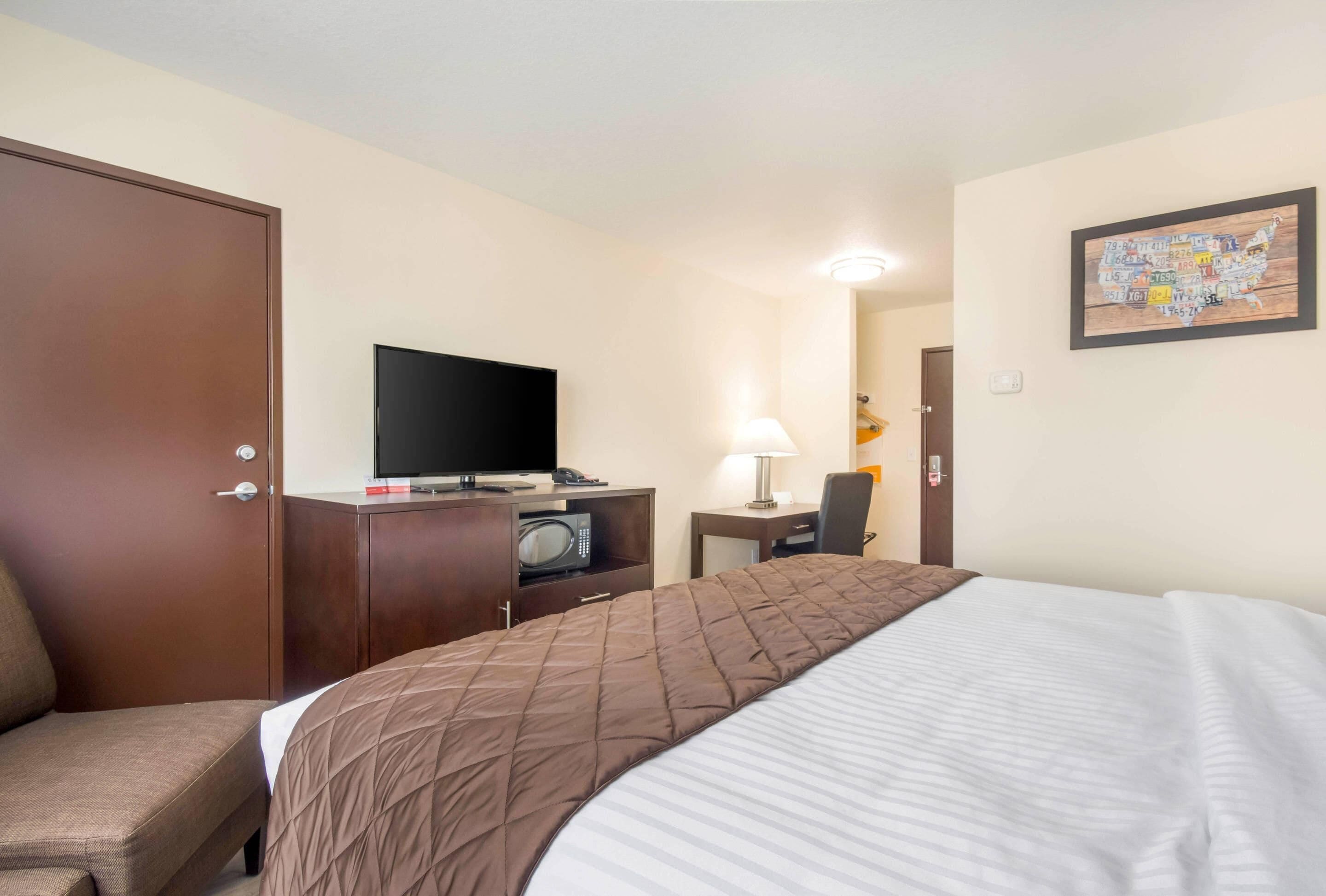 A hotel room with a bed, a desk with a computer, a television, a microwave, a chair, and a door.