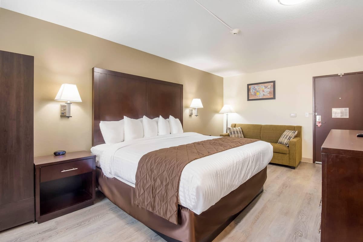 Ein Hotelzimmer mit einem großen Bett, Nachttischlampen, einem Nachtisch, einer Couch und einem Holzschrank.