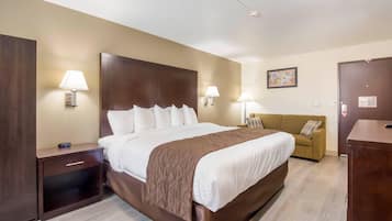 A hotel room with a large bed, bedside lamps, a nightstand, a sofa, and a wooden wardrobe.