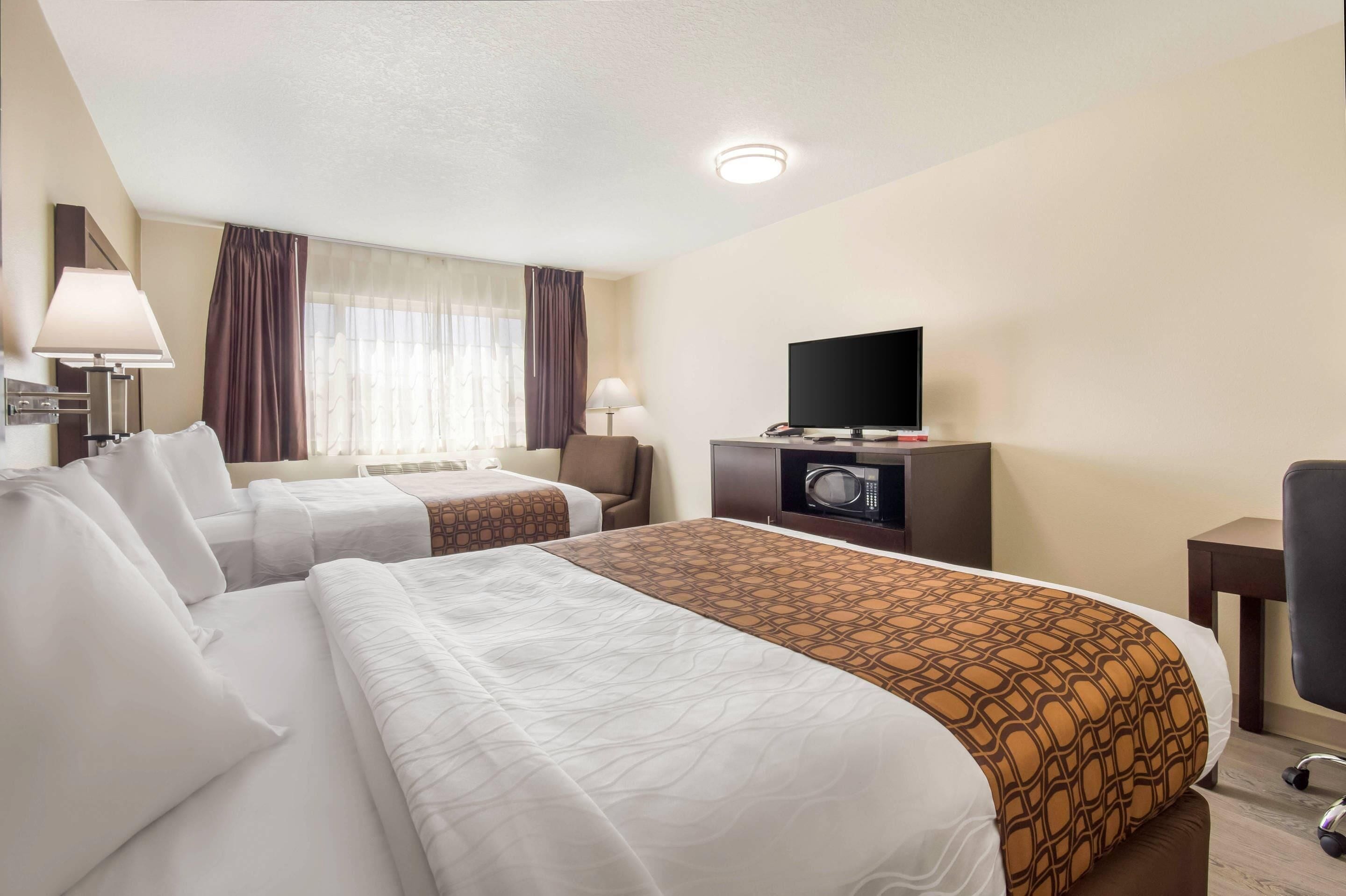 A hotel room with two beds, a television, a microwave, and a desk.