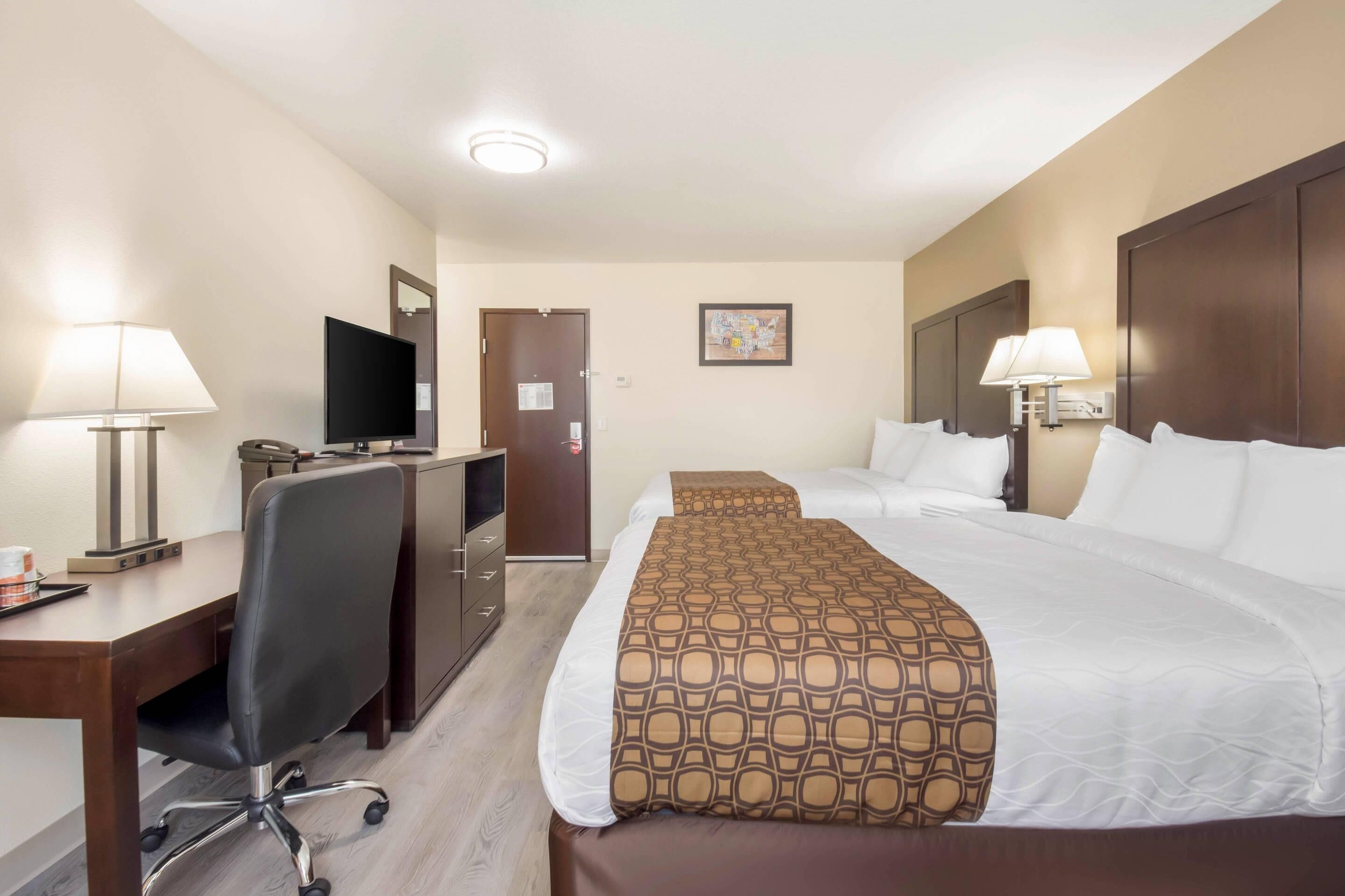 Habitación de hotel con cama, escritorio, silla, televisión y dos lámparas.