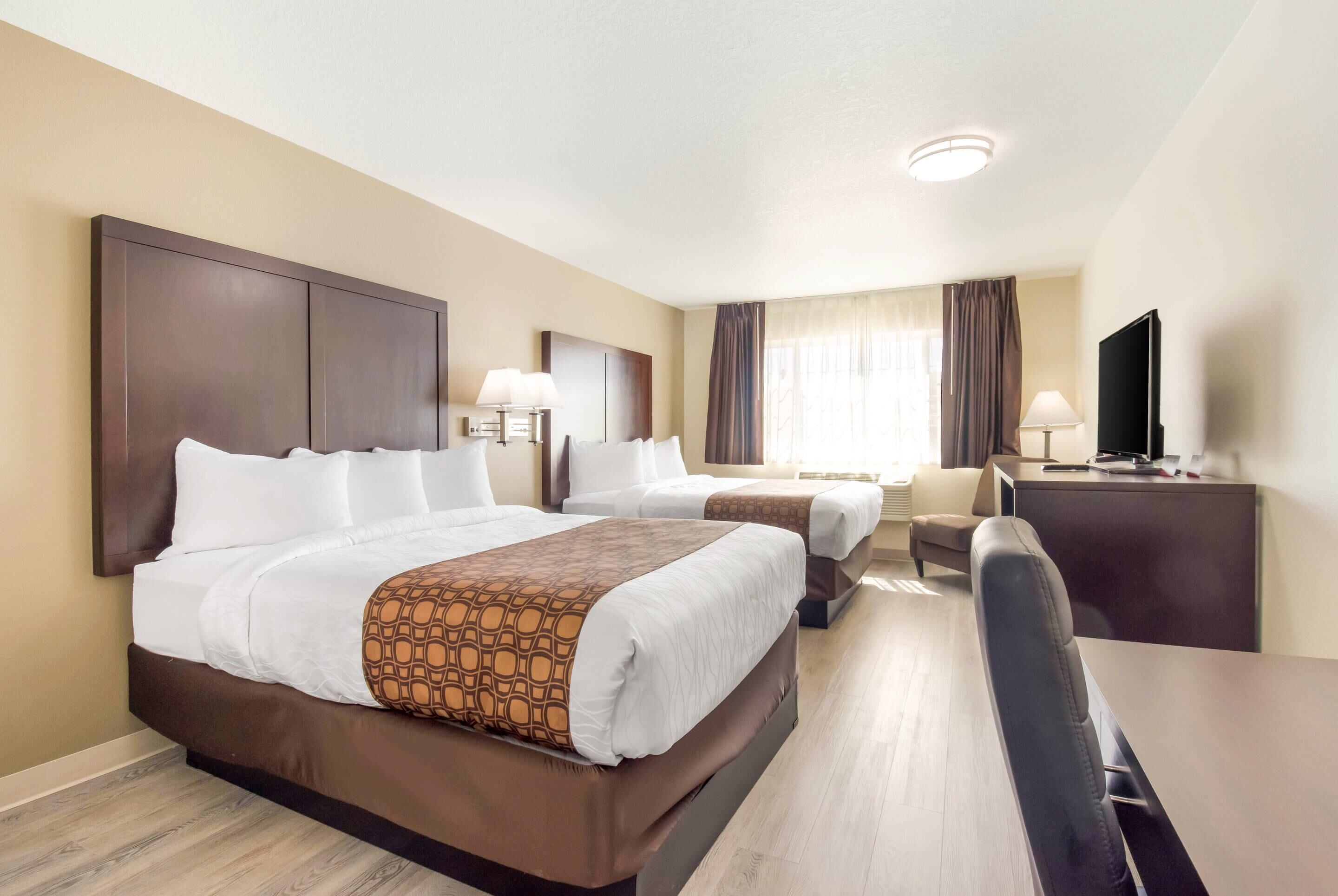 A hotel room with two beds, a desk, a chair, a TV, and a window with curtains.