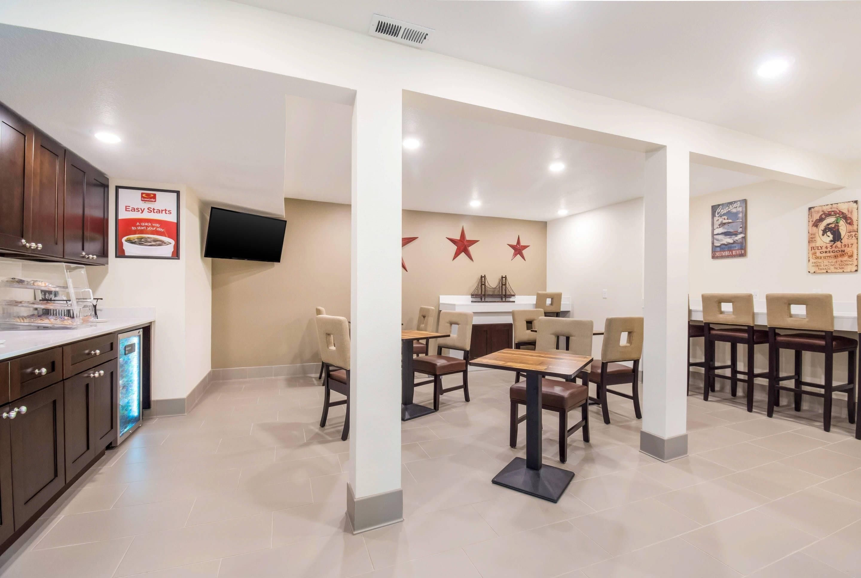 Un espace repas moderne avec une table centrale et des chaises, un coin cuisine doté de placards et d’un réfrigérateur, et un téléviseur fixé au mur.