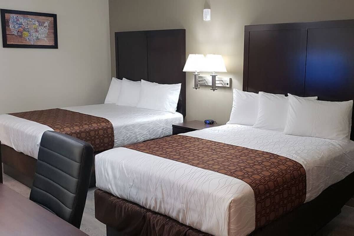 Ein Hotelzimmer mit zwei Betten, einem Schreibtisch, einem Stuhl, einer Lampe und einer Tür.