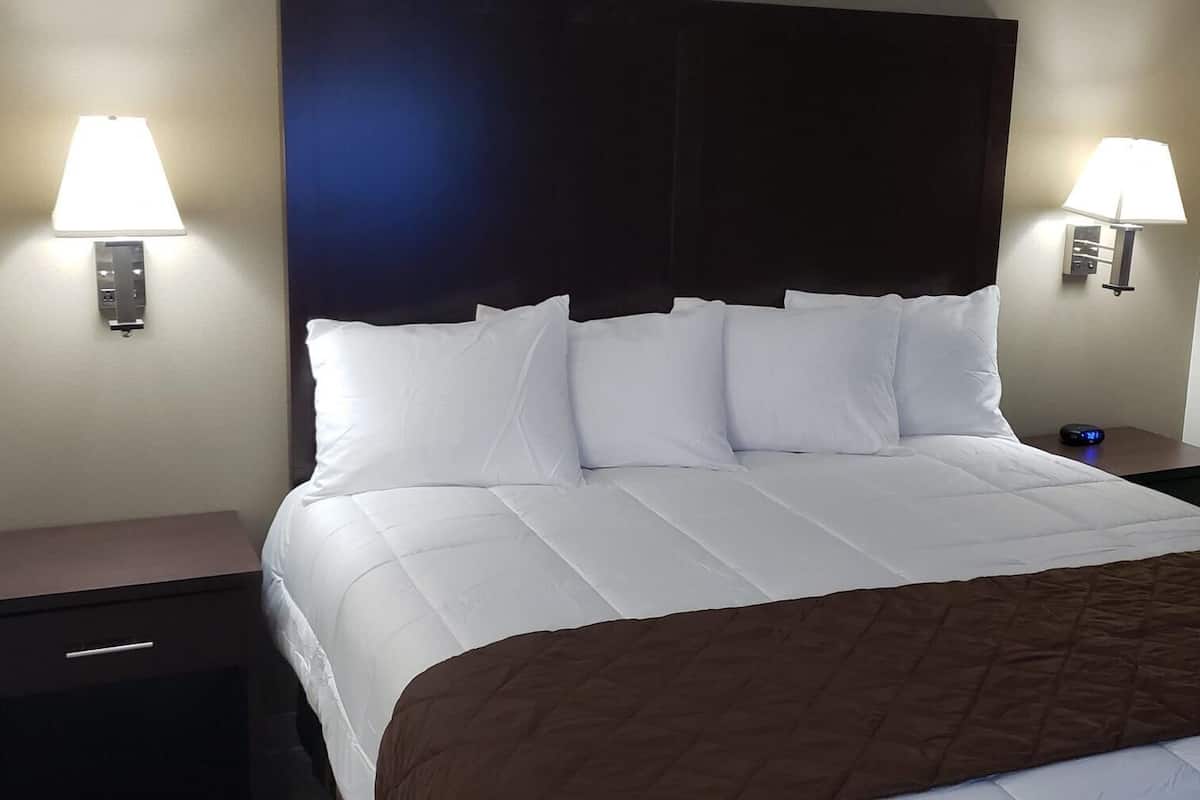 Ein Hotelzimmer mit einem Bett, zwei Nachttischen, einer Lampe und einem Fenster mit Jalousien.