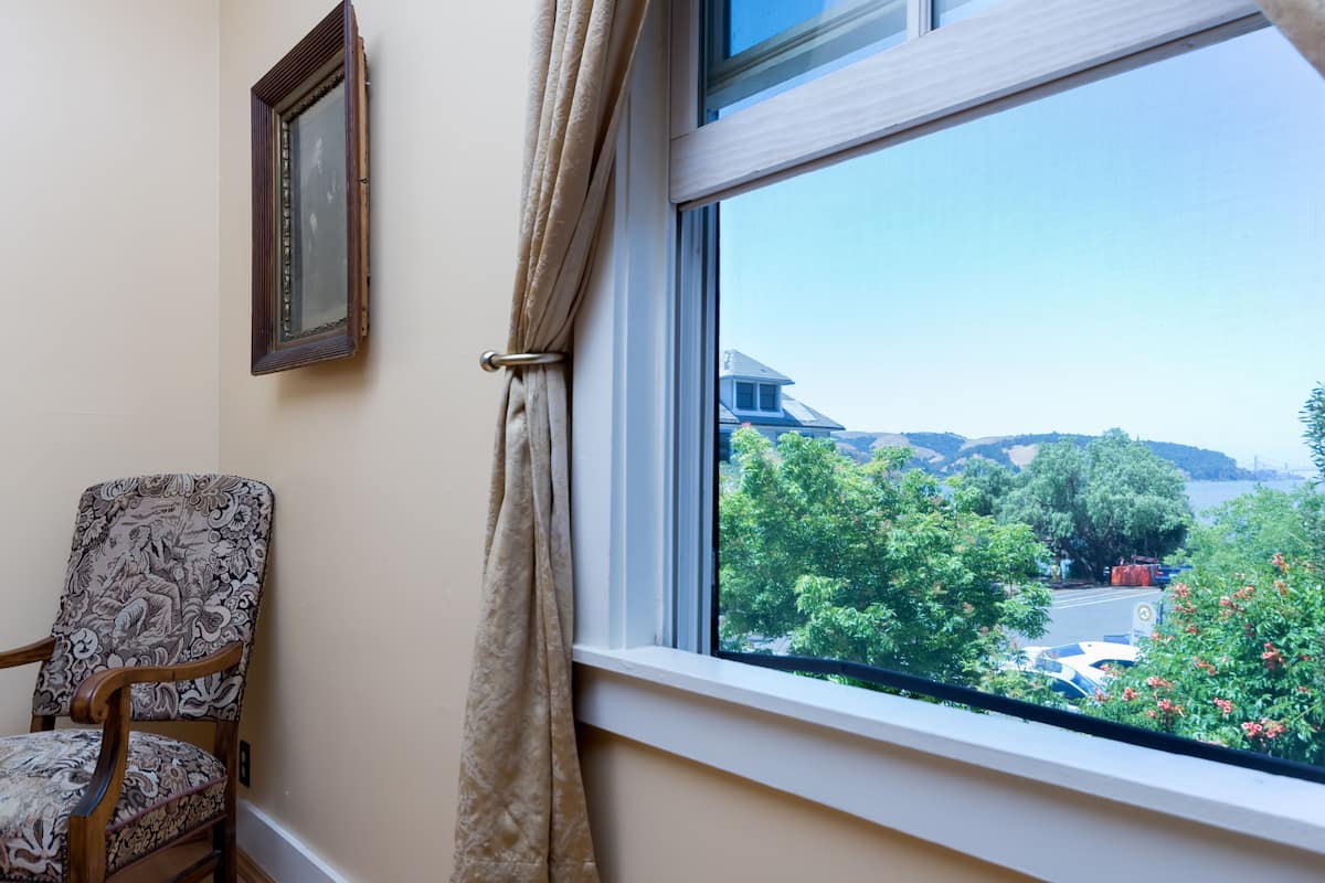 Una habitación con ventana que da a una zona residencial, una silla y un cuadro en la pared.