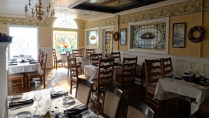 Un comedor con varias mesas y sillas, una araña y elementos decorativos como coronas y vidrieras.