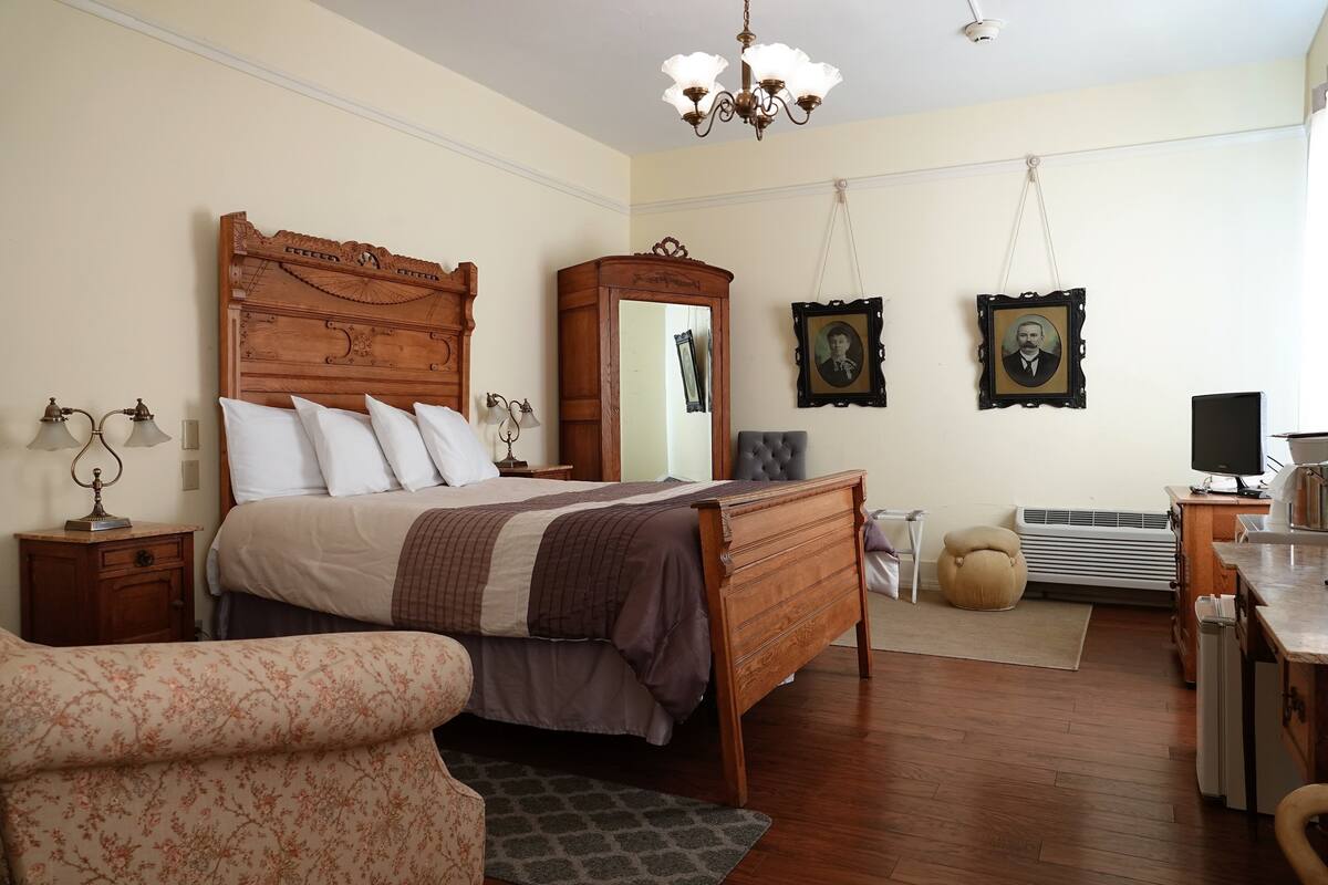 Un dormitorio con una cama de madera, una mesita de noche, un aparador, un espejo y un escritorio con una computadora.