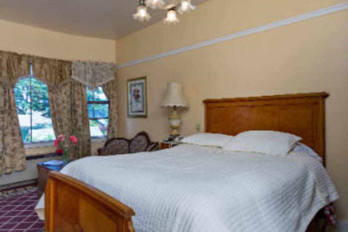 Un dormitorio con cama de madera, ventana con cortinas, un cuadro en la pared y una lámpara en una mesita de noche.