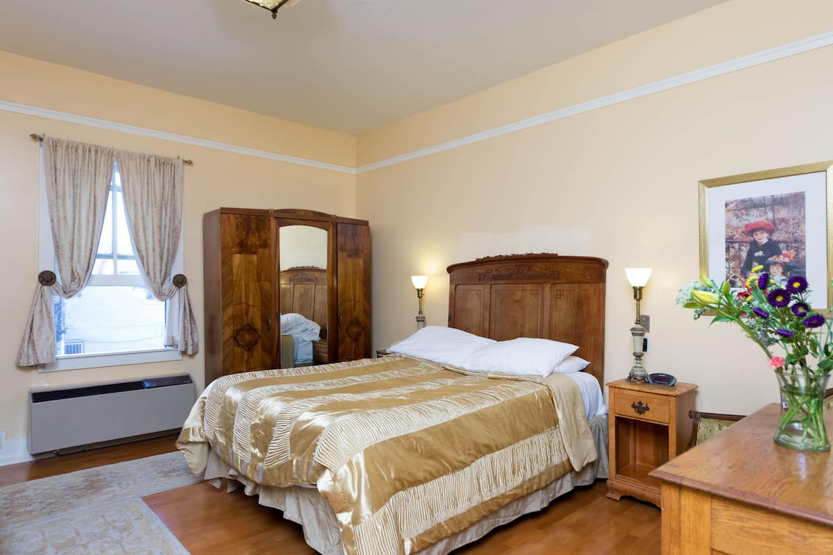 Un dormitorio con una cama grande, un armario de madera, una mesita de noche con una lámpara y una foto enmarcada en la pared.