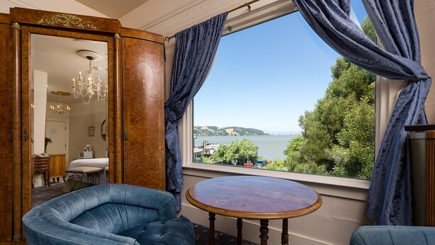 Una habitación con vista a un cuerpo de agua, una mesa redonda de madera y dos sillas tapizadas en azul.