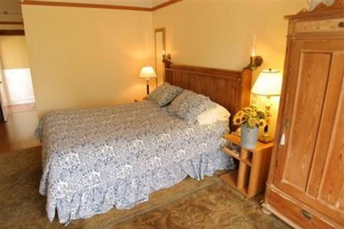 Un dormitorio con una cama, dos lámparas de noche, un armario de madera y un arreglo floral en la mesita de noche.
