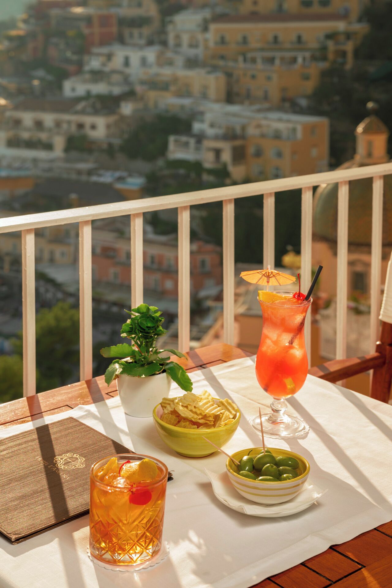 Una mesa con bebidas y aperitivos en un balcón con vistas a un paisaje urbano.