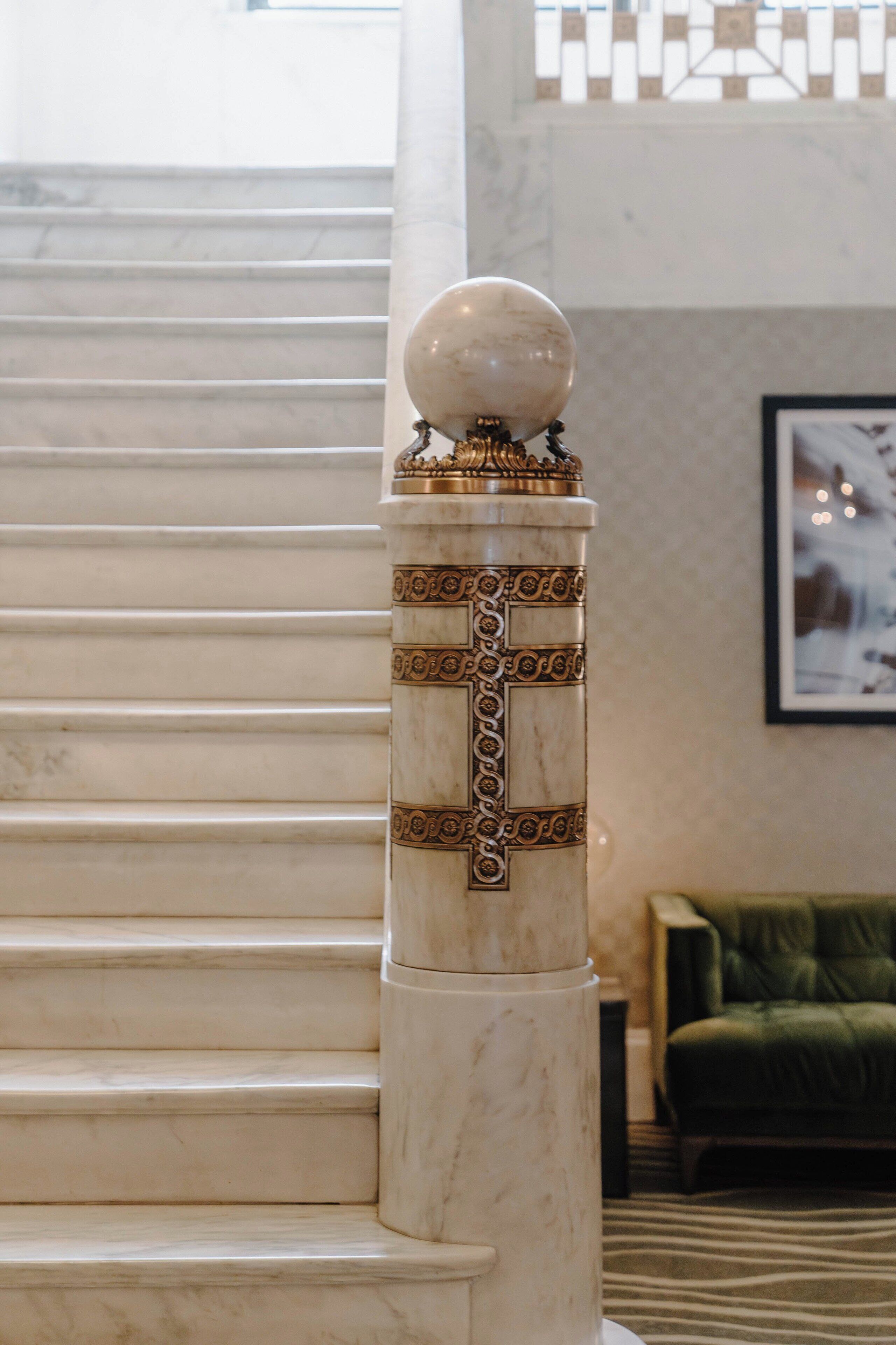 A marble staircase with a decorative column featuring a spherical top and a cross design.
