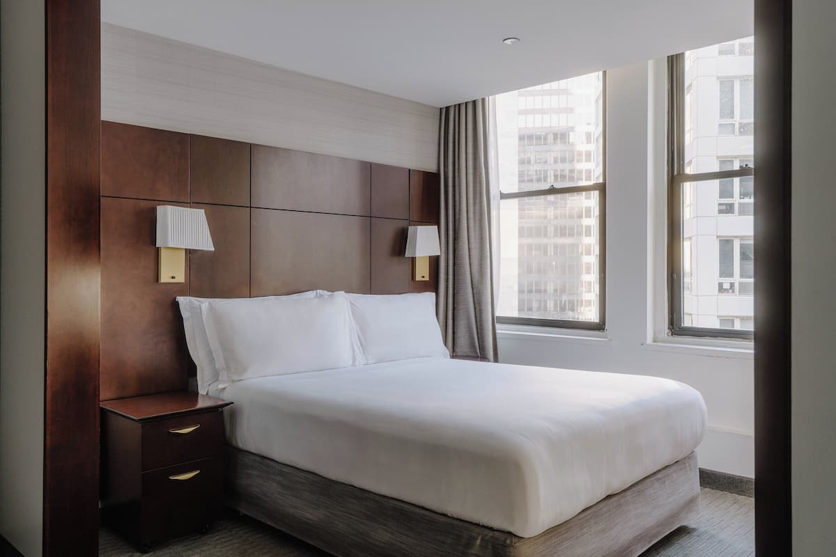 Ein Hotelzimmer mit einem großen Bett, zwei Nachttischen und einem Fenster mit Blick auf die Stadt.
