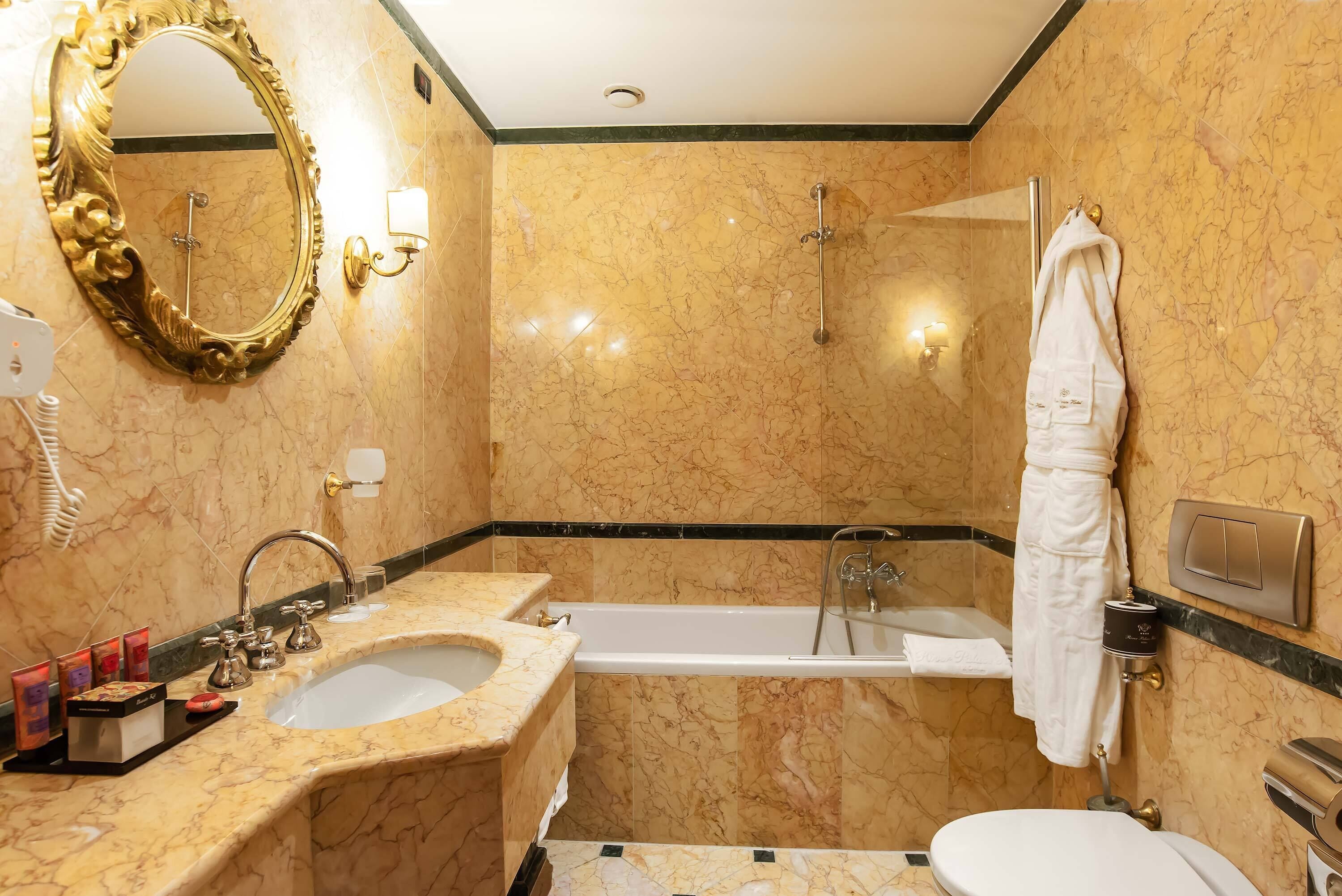 Une salle de bain avec un lavabo en marbre, une baignoire, des toilettes, une douche et un grand miroir.