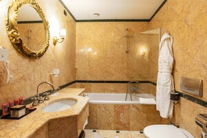 Et badeværelse med vask i marmor, badekar, toilet, bruser og et stort spejl.