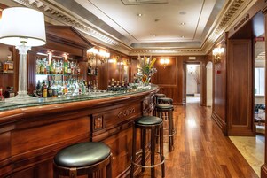 A bar area with a wooden counter, multiple stools, and a variety of bottles.