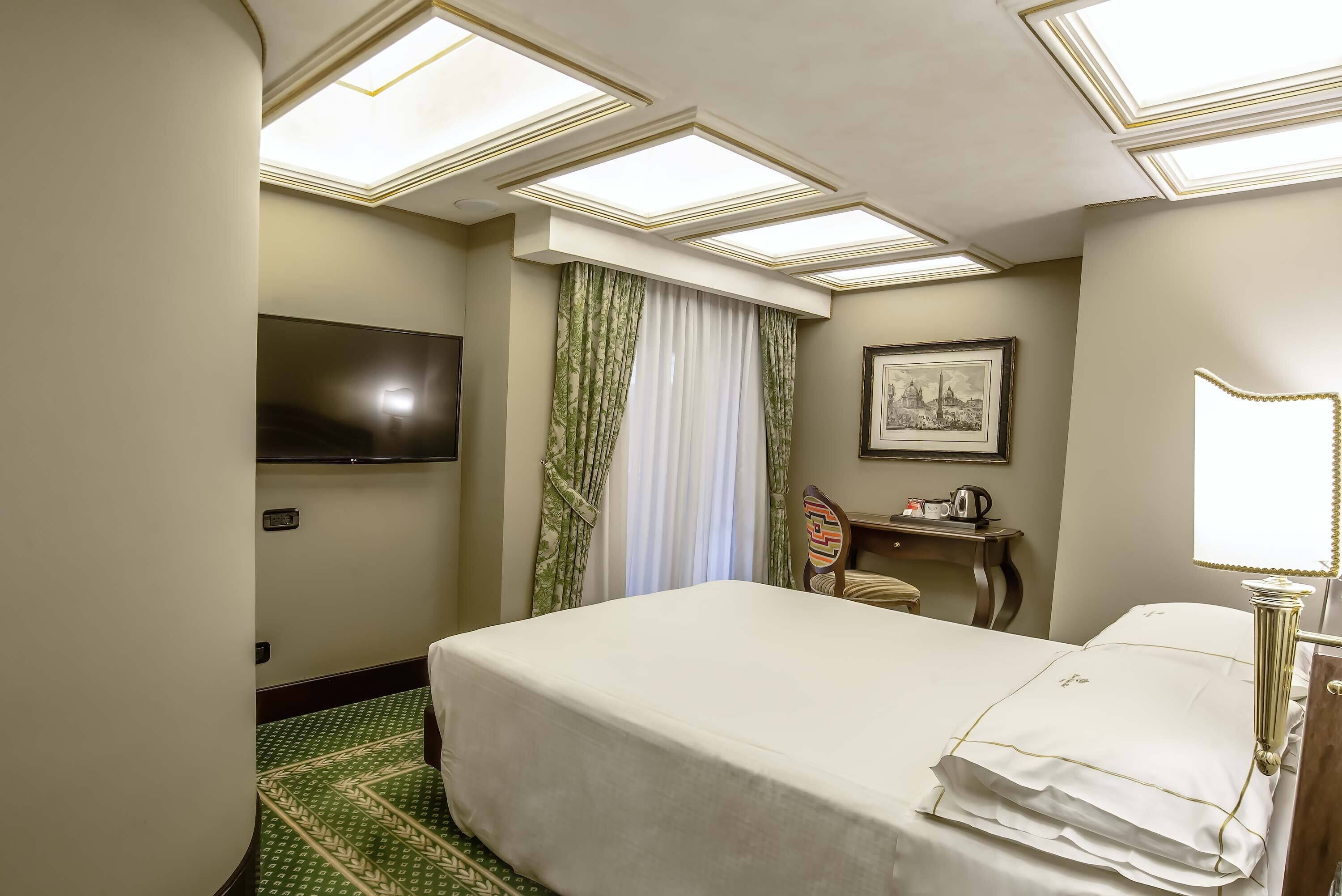 A hotel room with a bed, a desk, a chair, a television, and a picture on the wall.