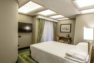 A hotel room with a bed, a desk, a chair, a television, and a picture on the wall.