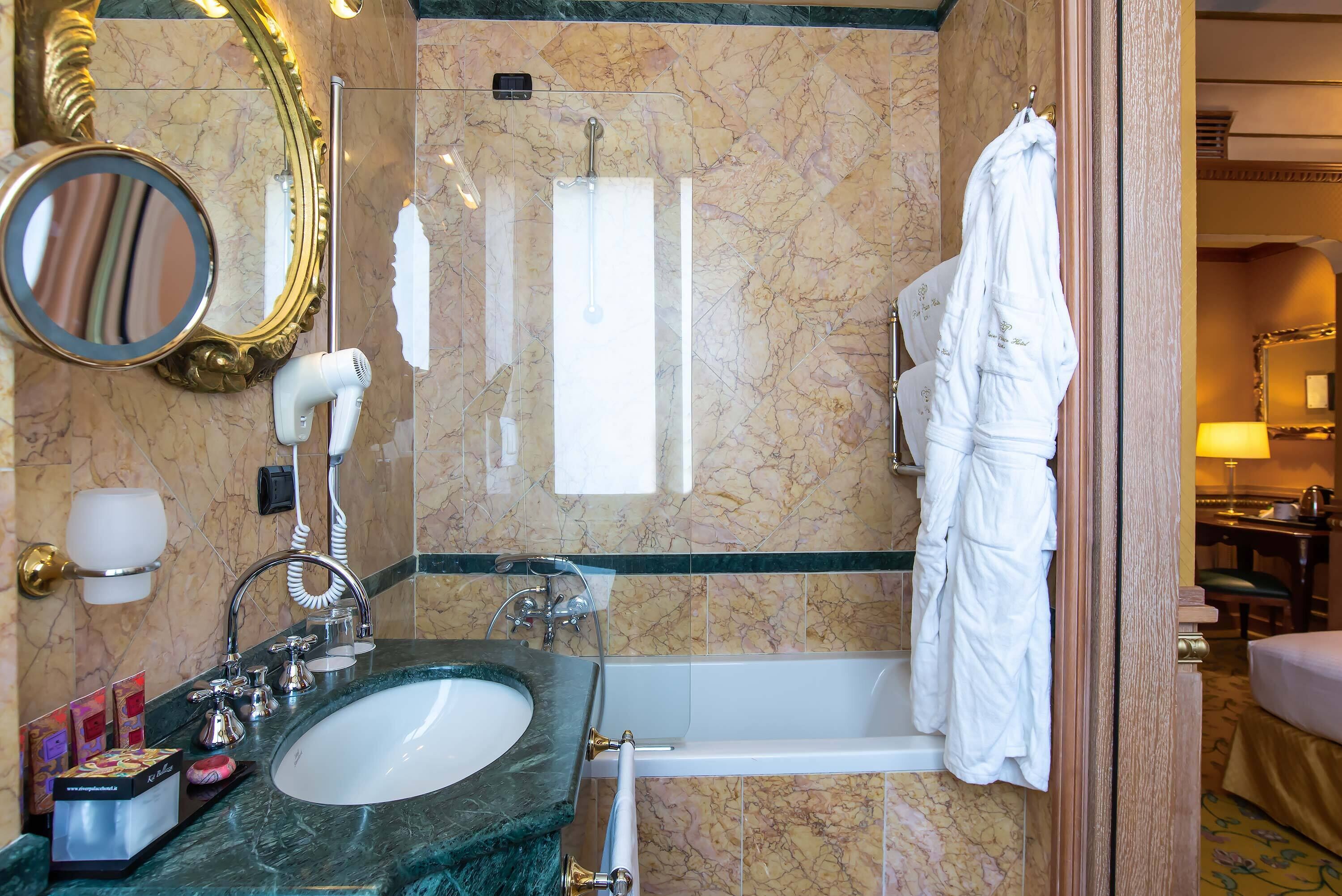 A bathroom with a marble sink, a bathtub, a mirror, a towel rack, and a robe hanging on the wall.