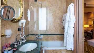 Un baño con lavamanos de mármol, bañera, espejo, toallero y bata colgada en la pared.