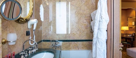 Un baño con lavamanos de mármol, bañera, espejo, toallero y bata colgada en la pared.